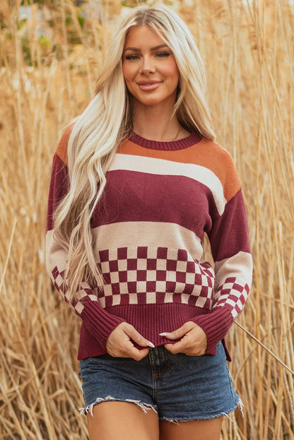 Woman wearing a burgundy, beige, and orange striped and checkered knit sweater with denim shorts, standing outdoors in tall dry grass.