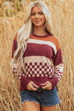 Woman wearing a burgundy, beige, and orange striped and checkered knit sweater with denim shorts, standing outdoors in tall dry grass.
