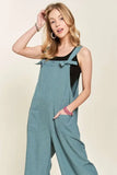 Woman wearing relaxed blue overalls with tie straps over a black tank top, posing casually.
