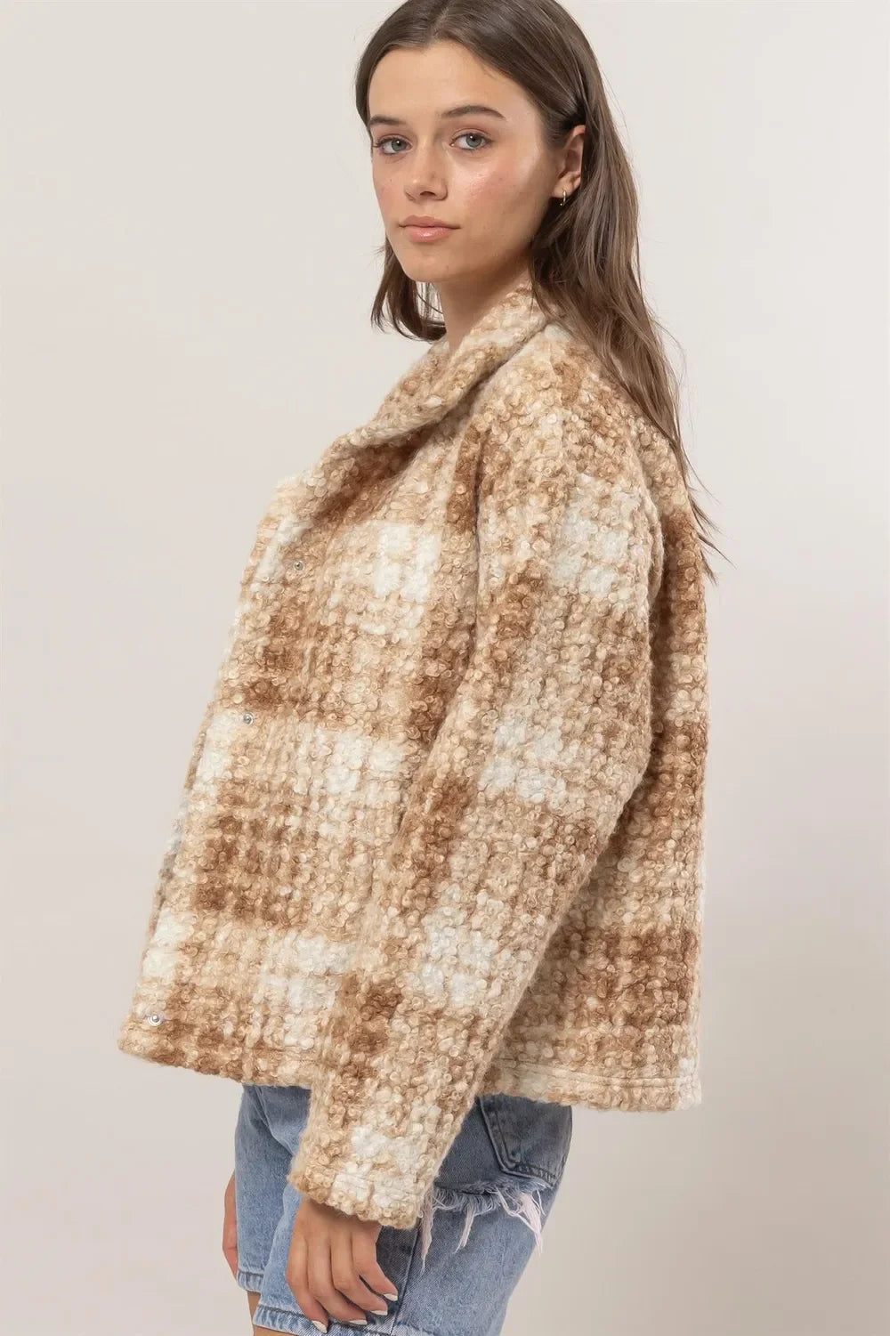 Woman wearing a textured beige plaid jacket with relaxed fit and distressed denim shorts