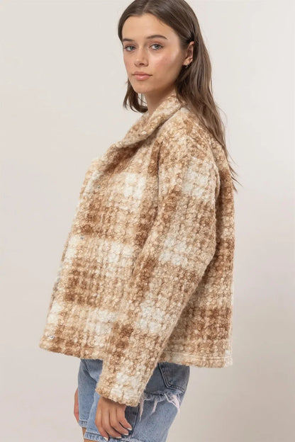 Woman wearing a textured beige plaid jacket with relaxed fit and distressed denim shorts