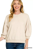 Woman wearing a relaxed fit sand beige sweatshirt with ribbed cuffs and blue jeans