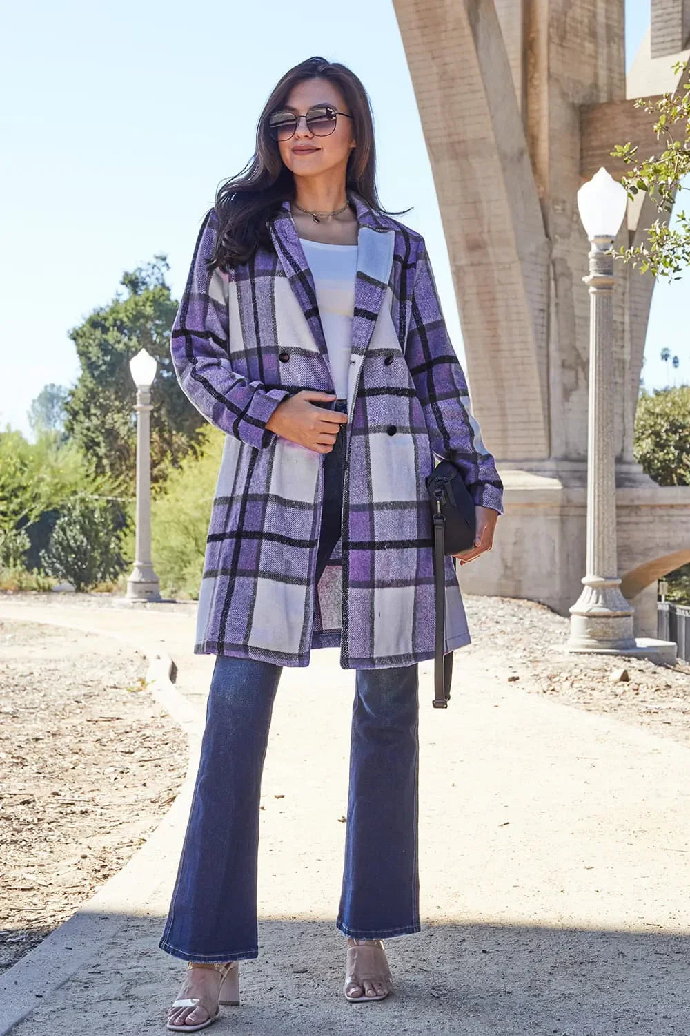 Woman wearing purple plaid coat, flared jeans, and sunglasses outdoors on a sunny day.
