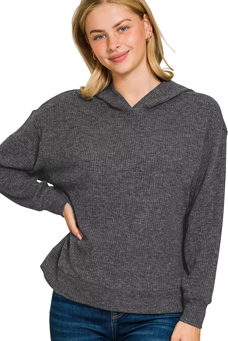 Woman wearing a textured black knit hoodie with relaxed fit and long sleeves, paired with jeans.