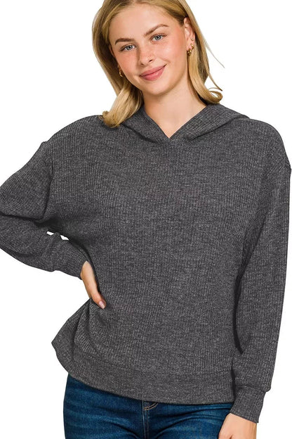 Woman wearing a textured black knit hoodie with relaxed fit and long sleeves, paired with jeans.