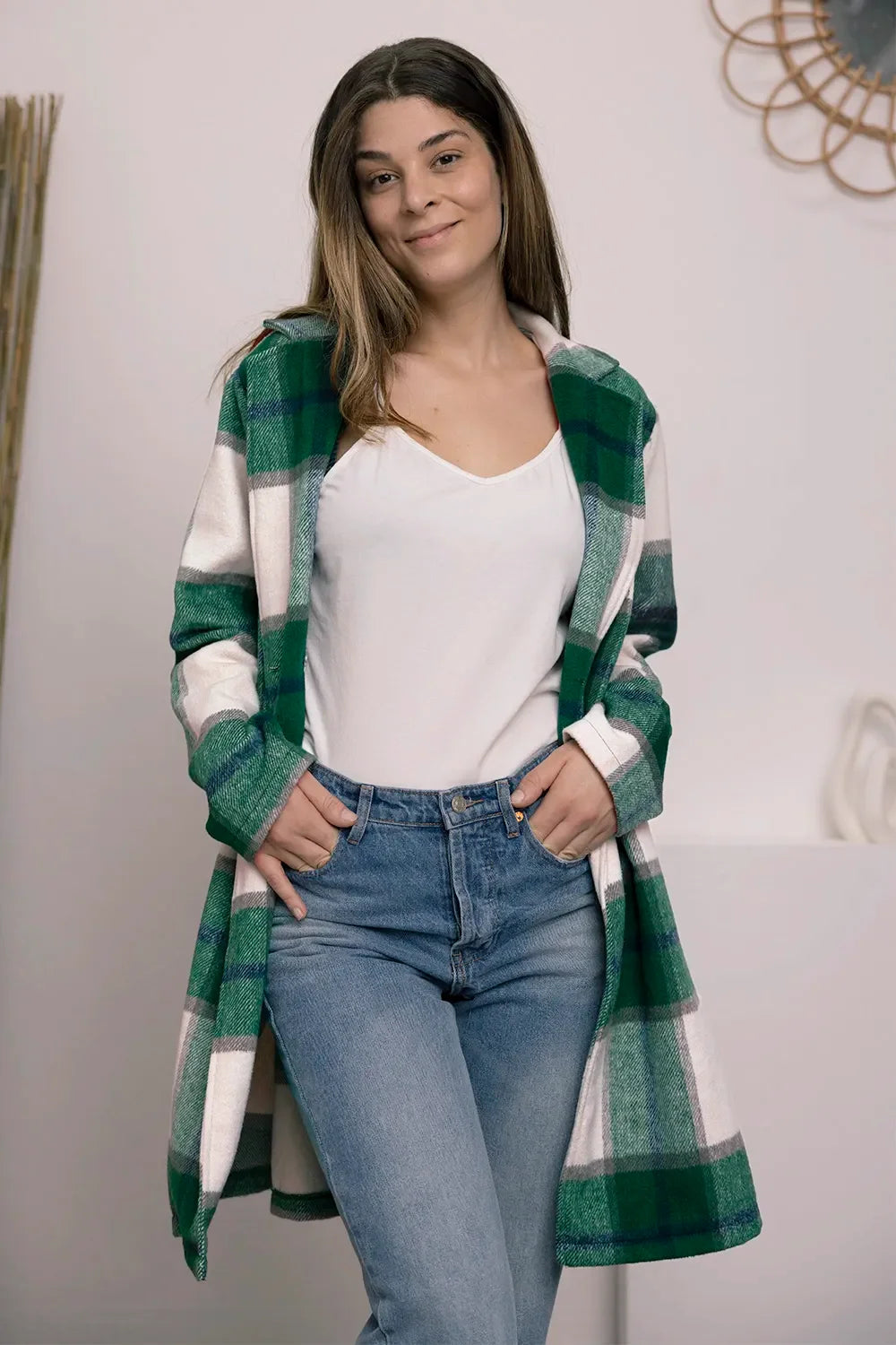 Woman wearing a green plaid open-front coat, white top, and blue jeans indoors
