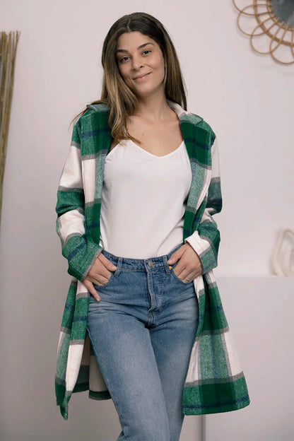 Woman wearing a green plaid open-front coat, white top, and blue jeans indoors