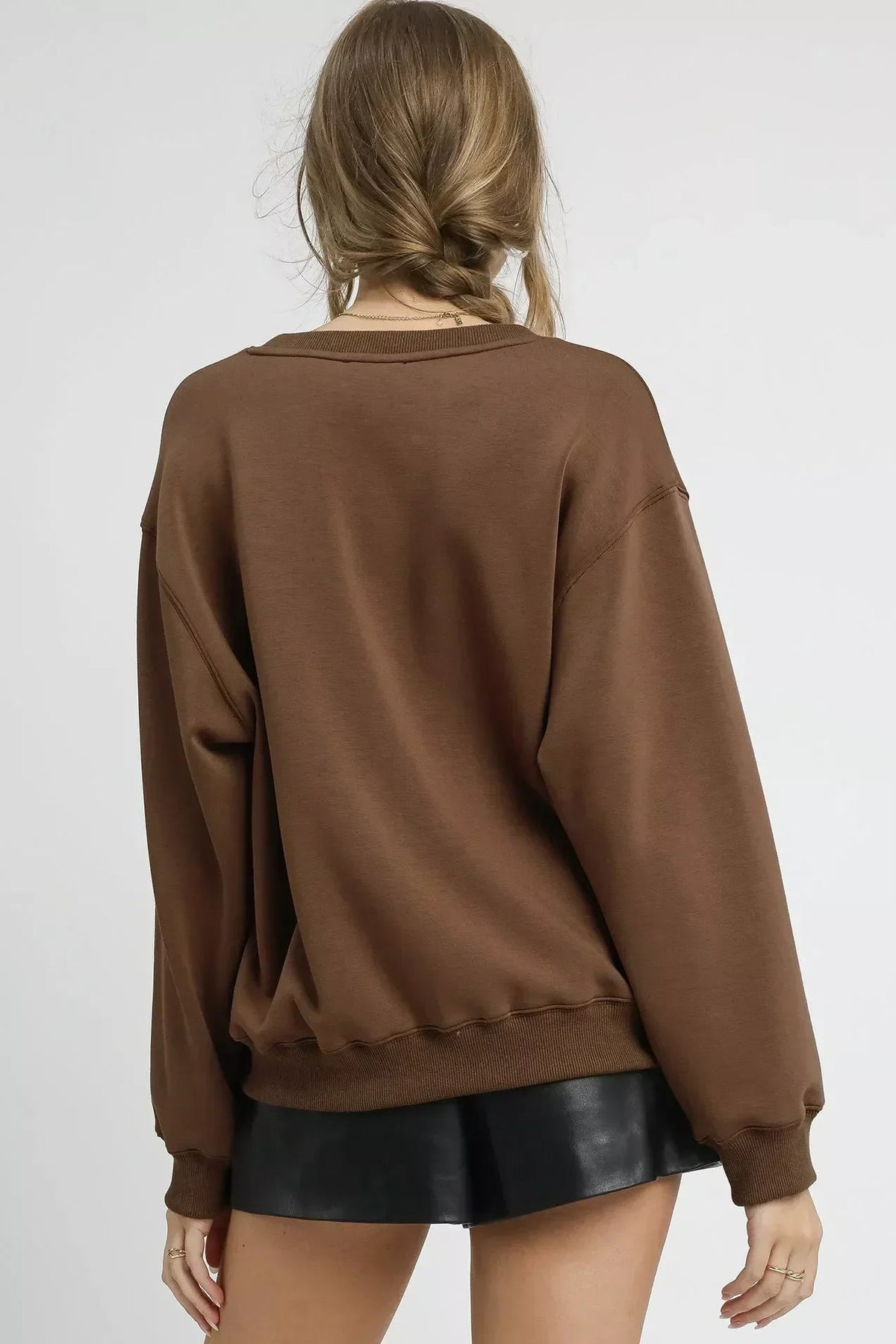 Woman wearing an oversized mocha brown sweatshirt and black faux leather shorts, back view