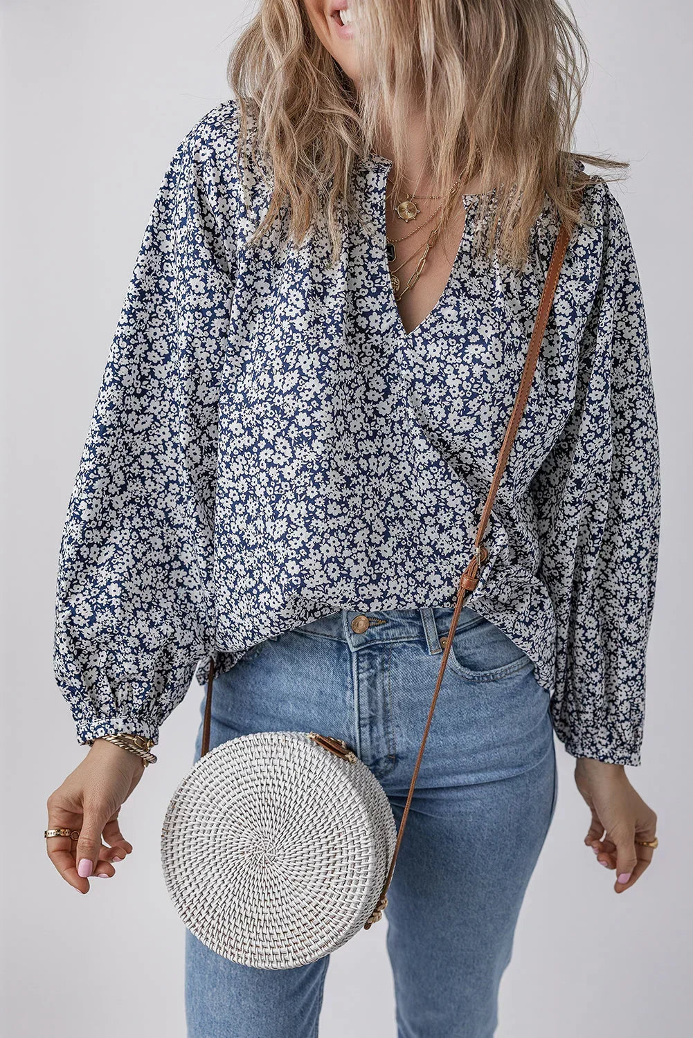 Woman wearing a blue floral blouse with balloon sleeves, light jeans, and a round woven crossbody bag