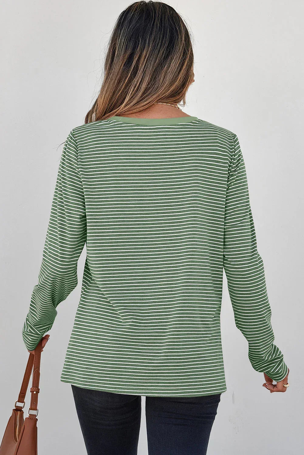 Woman wearing a green and white striped long sleeve top with dark jeans, back view