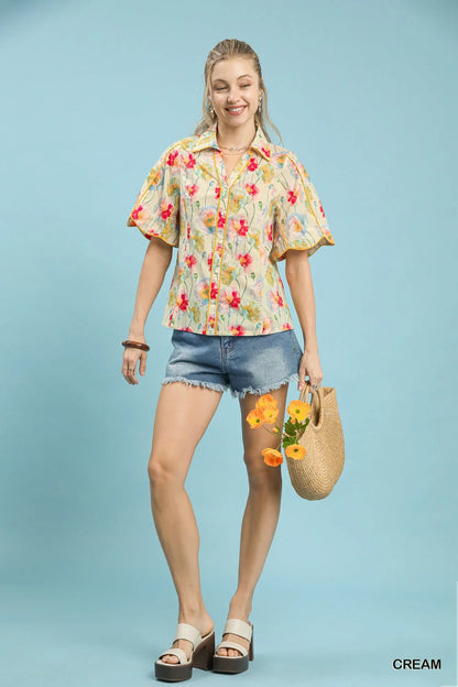Woman in floral short sleeve blouse and denim shorts holding straw bag with flowers