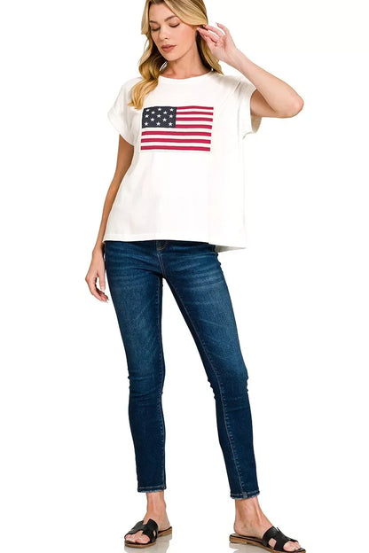 Woman wearing white t-shirt with American flag print, skinny blue jeans, and black sandals
