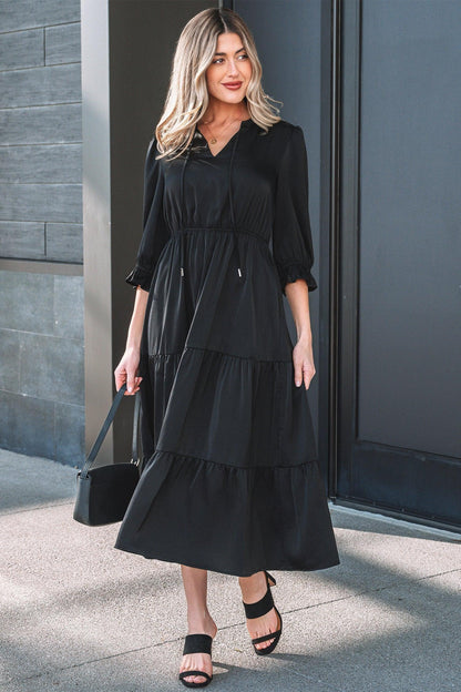 Woman in black tiered midi dress with three-quarter sleeves, holding a black handbag