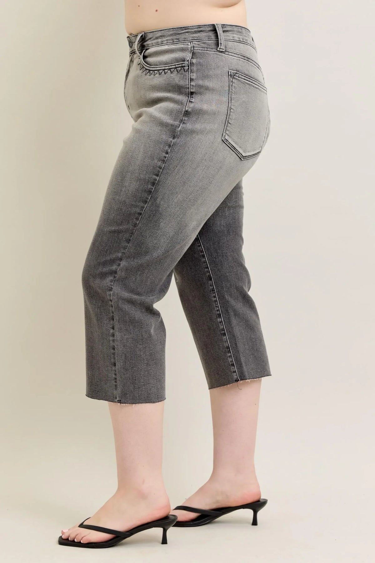 Woman wearing grey cropped denim jeans with raw hem and black heeled sandals
