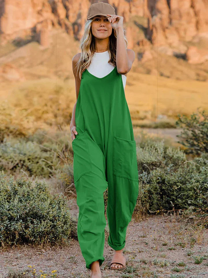 Woman in relaxed green jumpsuit and white tank top walking outdoors in a natural landscape