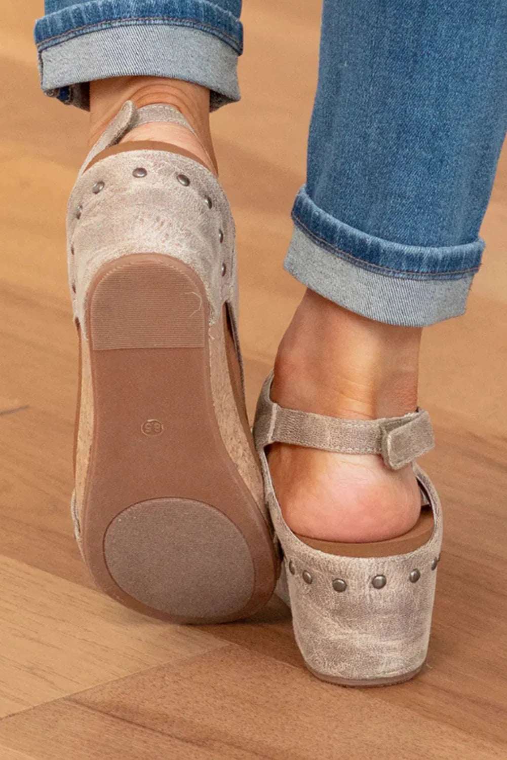 Close-up of woman wearing suede heeled clogs with metal studs and ankle strap on wooden floor