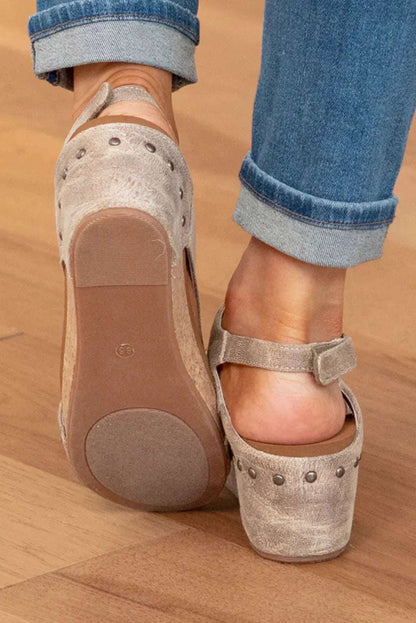 Close-up of woman wearing suede heeled clogs with metal studs and ankle strap on wooden floor