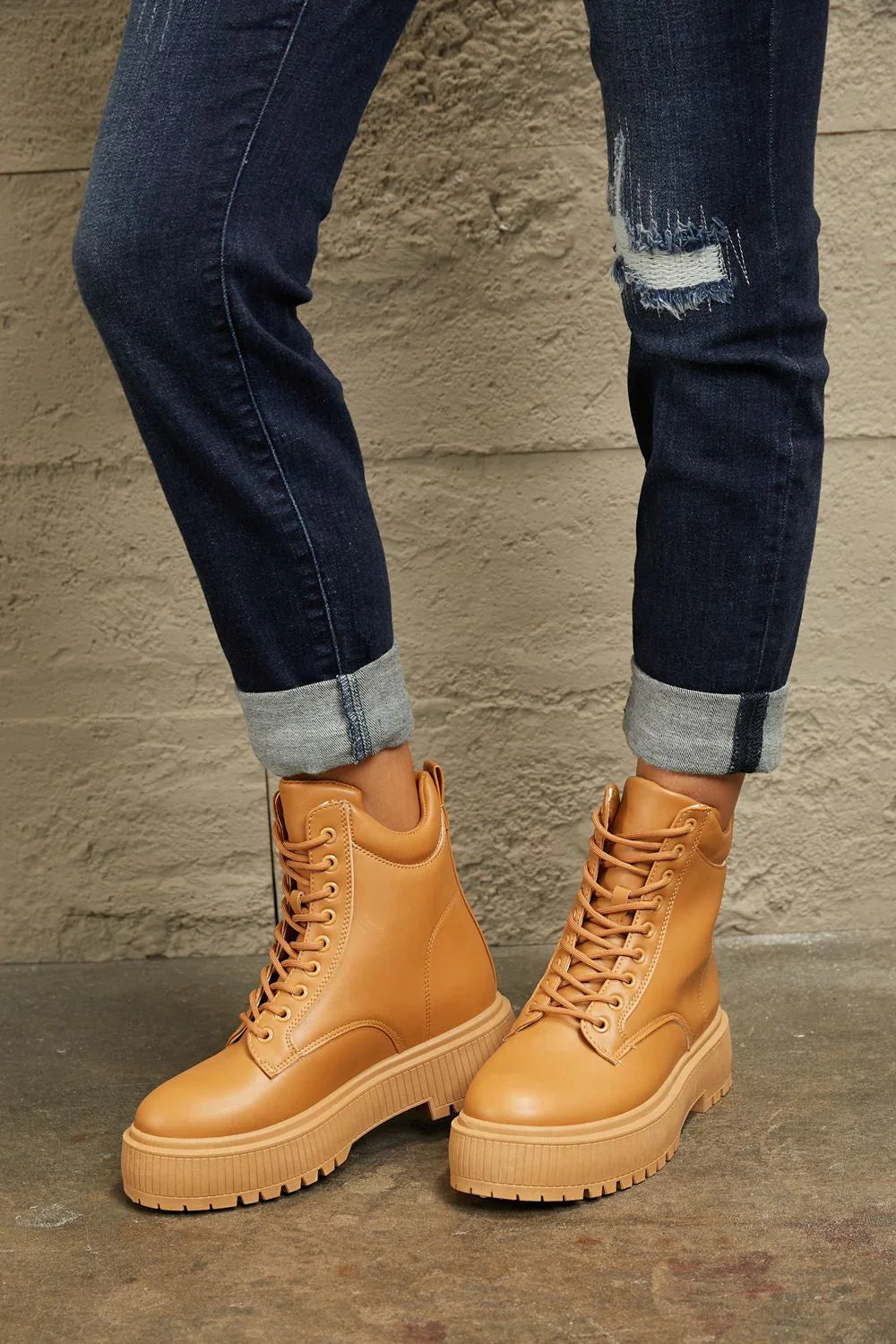 Tan lace-up platform boots paired with cuffed dark denim jeans on a textured floor