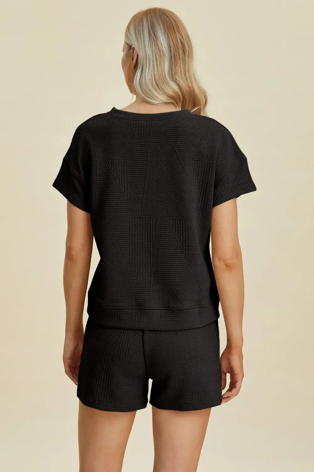 Woman wearing black textured short-sleeve top and shorts set, back view