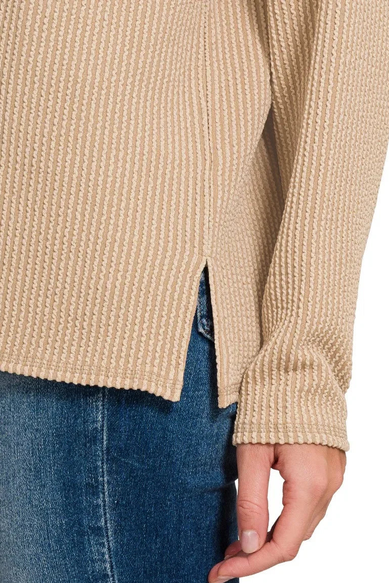 Close-up of textured light mocha waffle knit long sleeve top with side slit, styled with denim jeans.