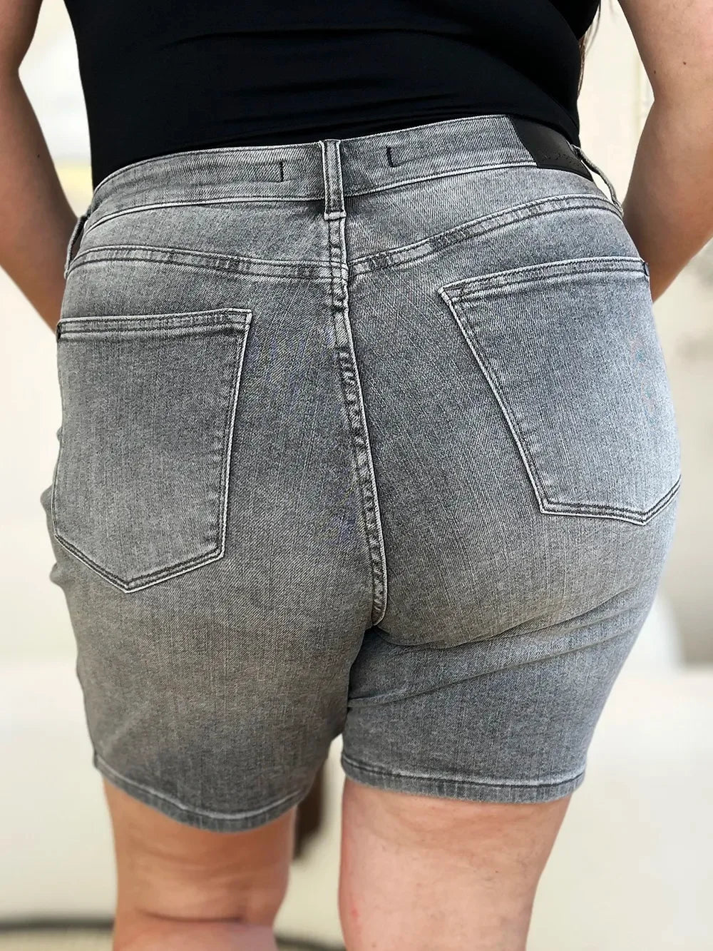 Back view of high-waisted grey denim shorts with large rear pockets, worn by a woman.