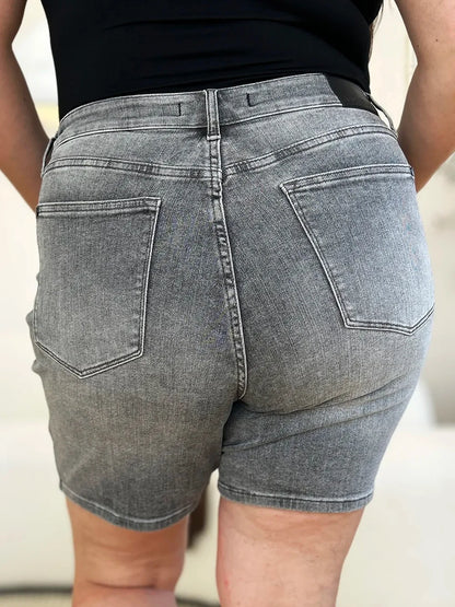 Back view of high-waisted grey denim shorts with large rear pockets, worn by a woman.