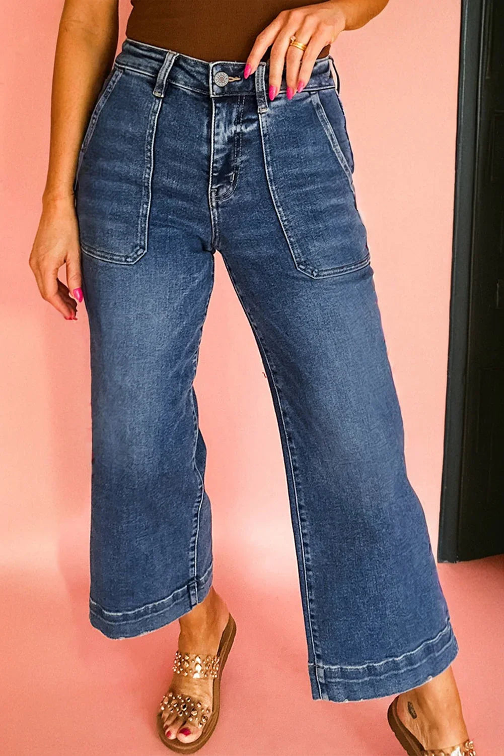 Woman wearing high-waisted wide-leg denim jeans with large front pockets and embellished sandals