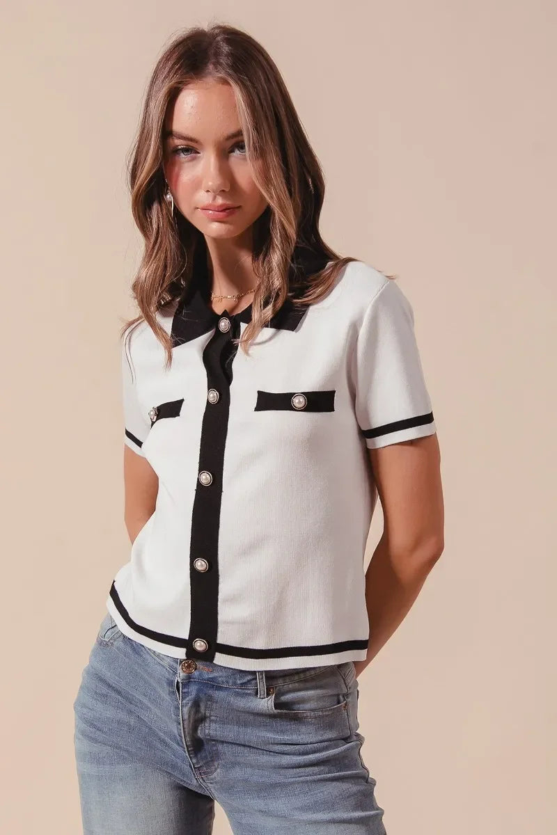 Woman wearing short sleeve white knit top with black trim and button details, blue jeans
