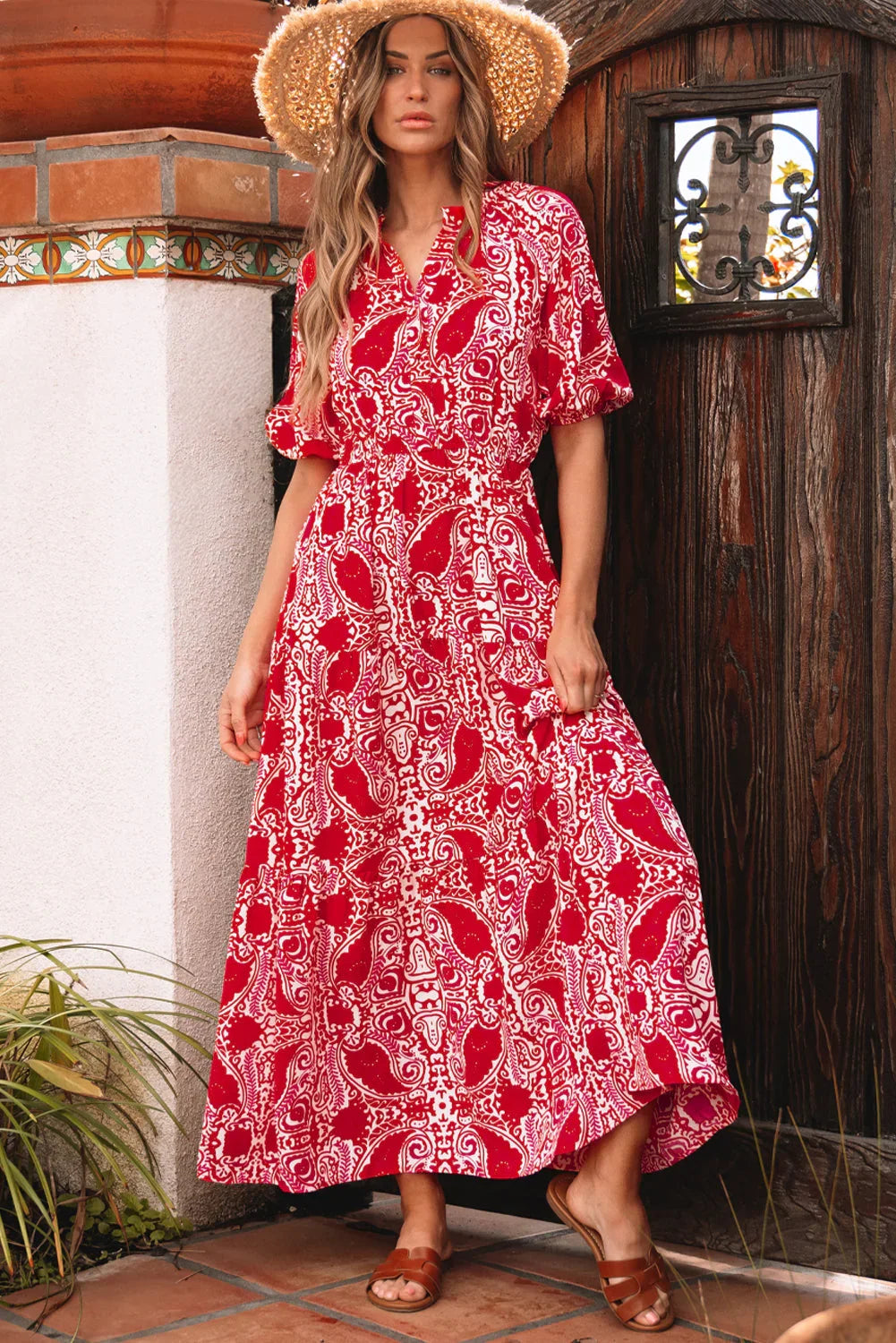 Woman in red and white paisley maxi dress with short sleeves and straw hat, standing outdoors