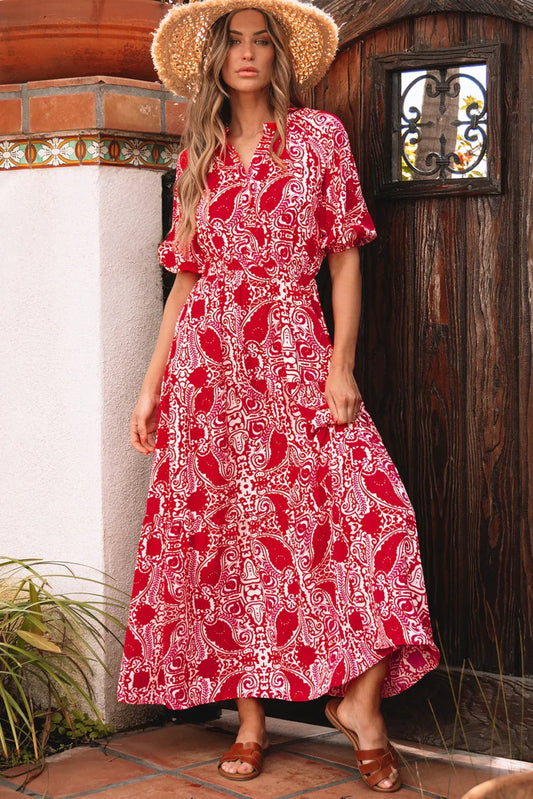 Woman in red and white paisley maxi dress with short sleeves and straw hat, standing outdoors