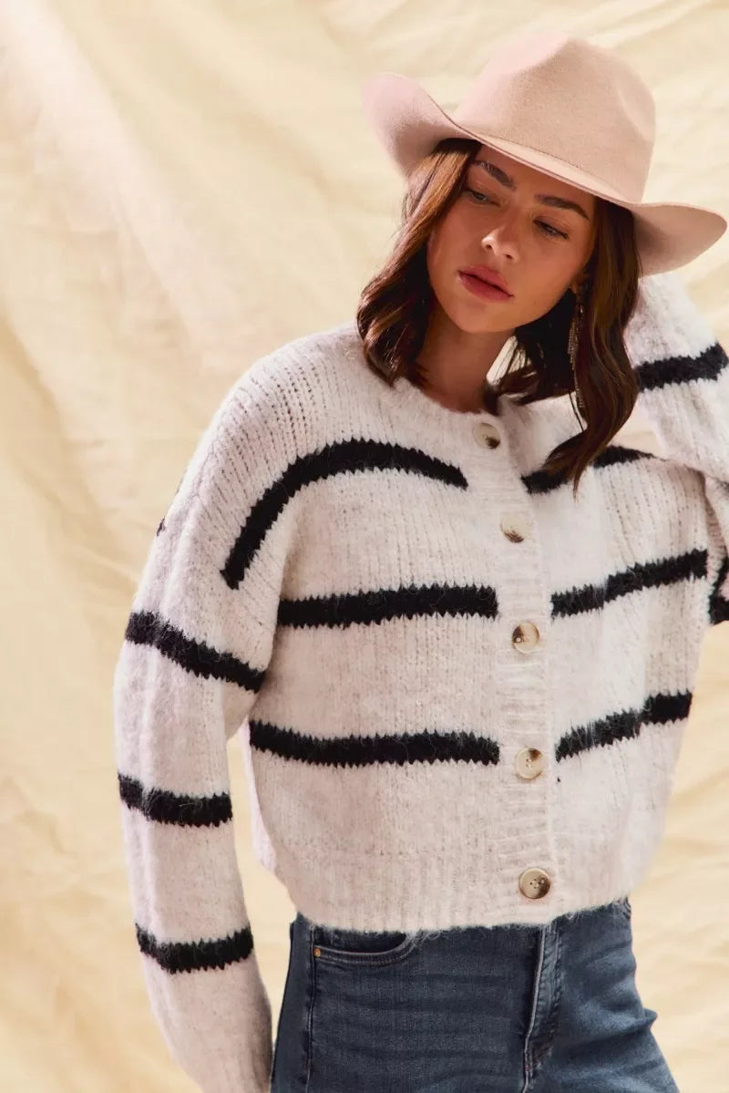 Woman wearing a cozy striped button-up sweater, wide-brim hat, and blue jeans.