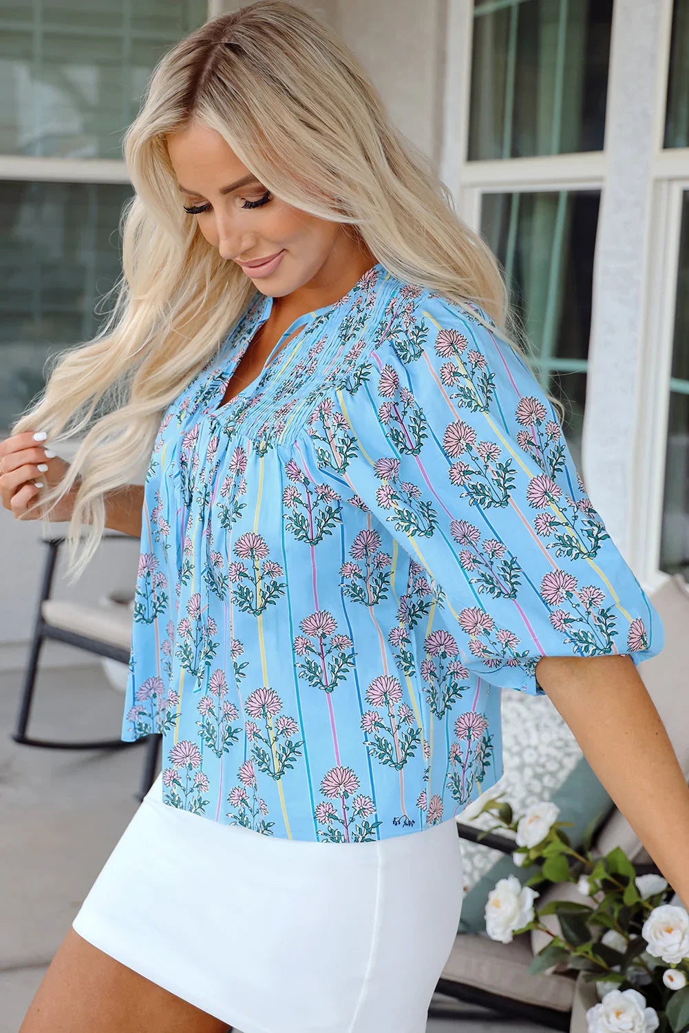 Woman wearing a blue floral blouse with puff sleeves and white mini skirt, outdoor patio setting.