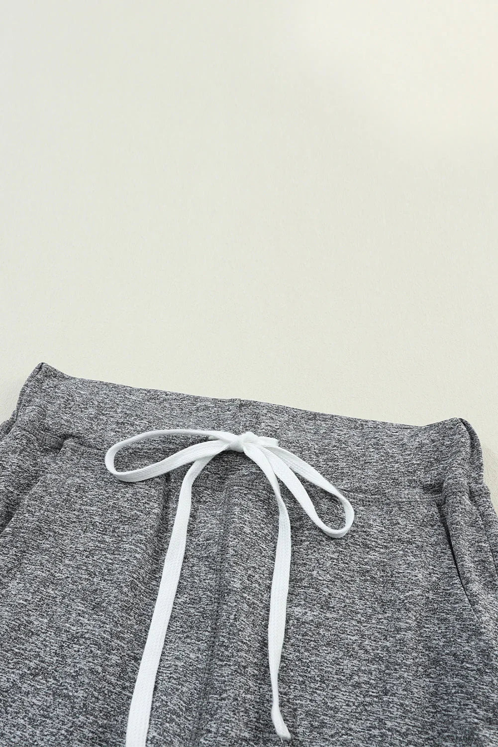 Close-up of heather grey knit joggers with white drawstring on a neutral background