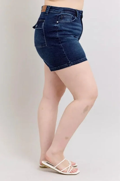 Woman in dark wash denim shorts and white sandals, side view against a light background.