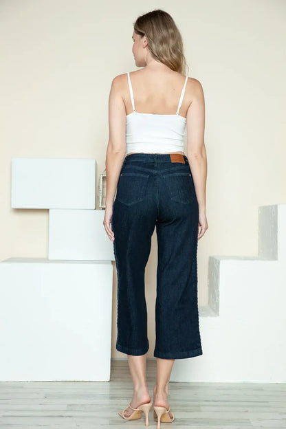 Woman in cropped dark wash wide-leg jeans and white tank top, rear view, indoor setting