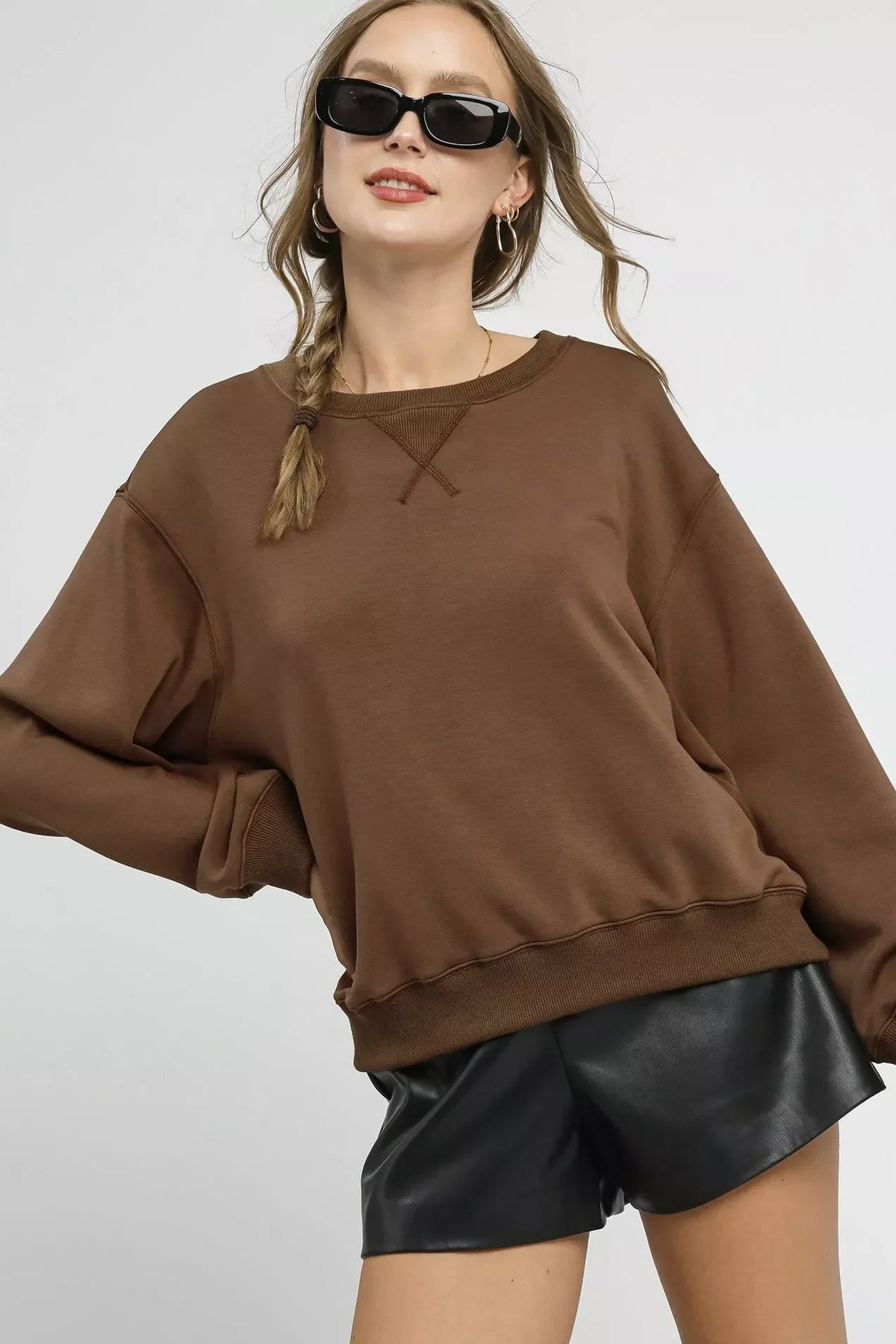 Woman in oversized brown sweatshirt and black faux leather shorts with sunglasses