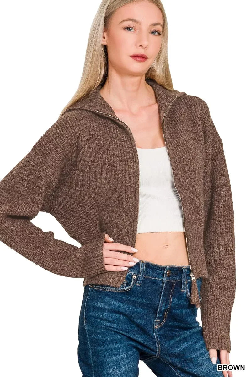 Woman wearing a brown ribbed zip-up cardigan, white crop top, and blue high-waisted jeans.