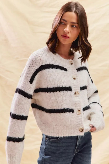 Woman wearing a white knit cardigan with black stripes and button front, paired with jeans