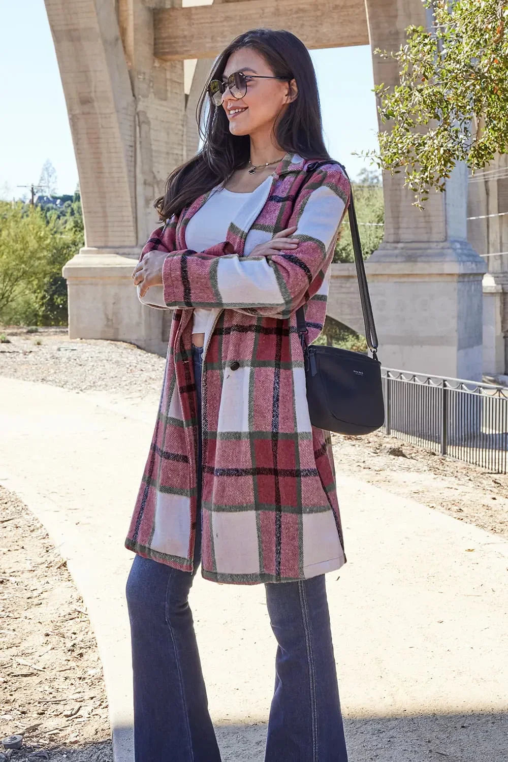 Woman outdoors wearing a pink plaid long coat, white top, flared jeans, and sunglasses