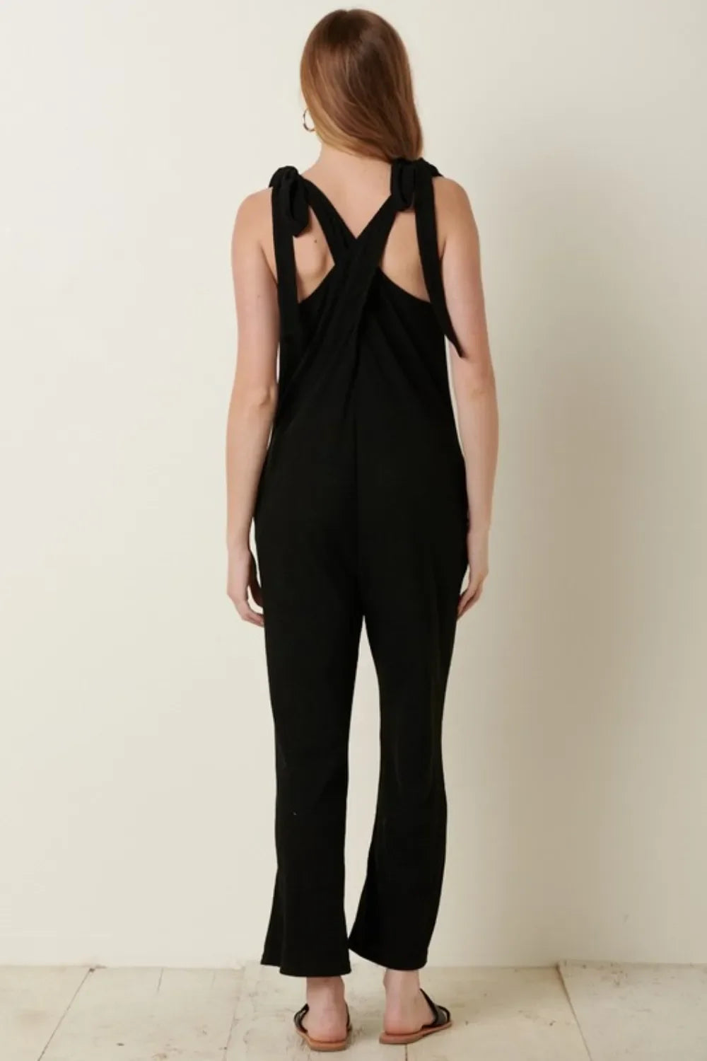 Woman wearing black sleeveless jumpsuit with tie straps, shown from the back