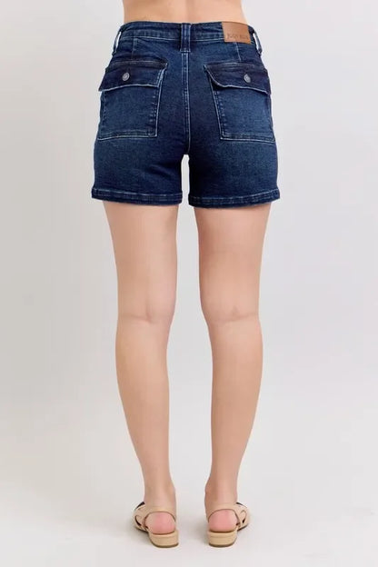 Back view of dark wash denim shorts with buttoned flap pockets and cuffed hem