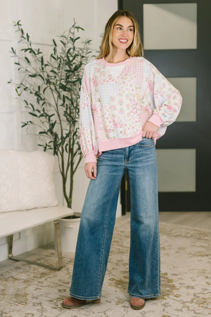 Woman wearing relaxed pink floral patchwork sweater and wide leg jeans indoors