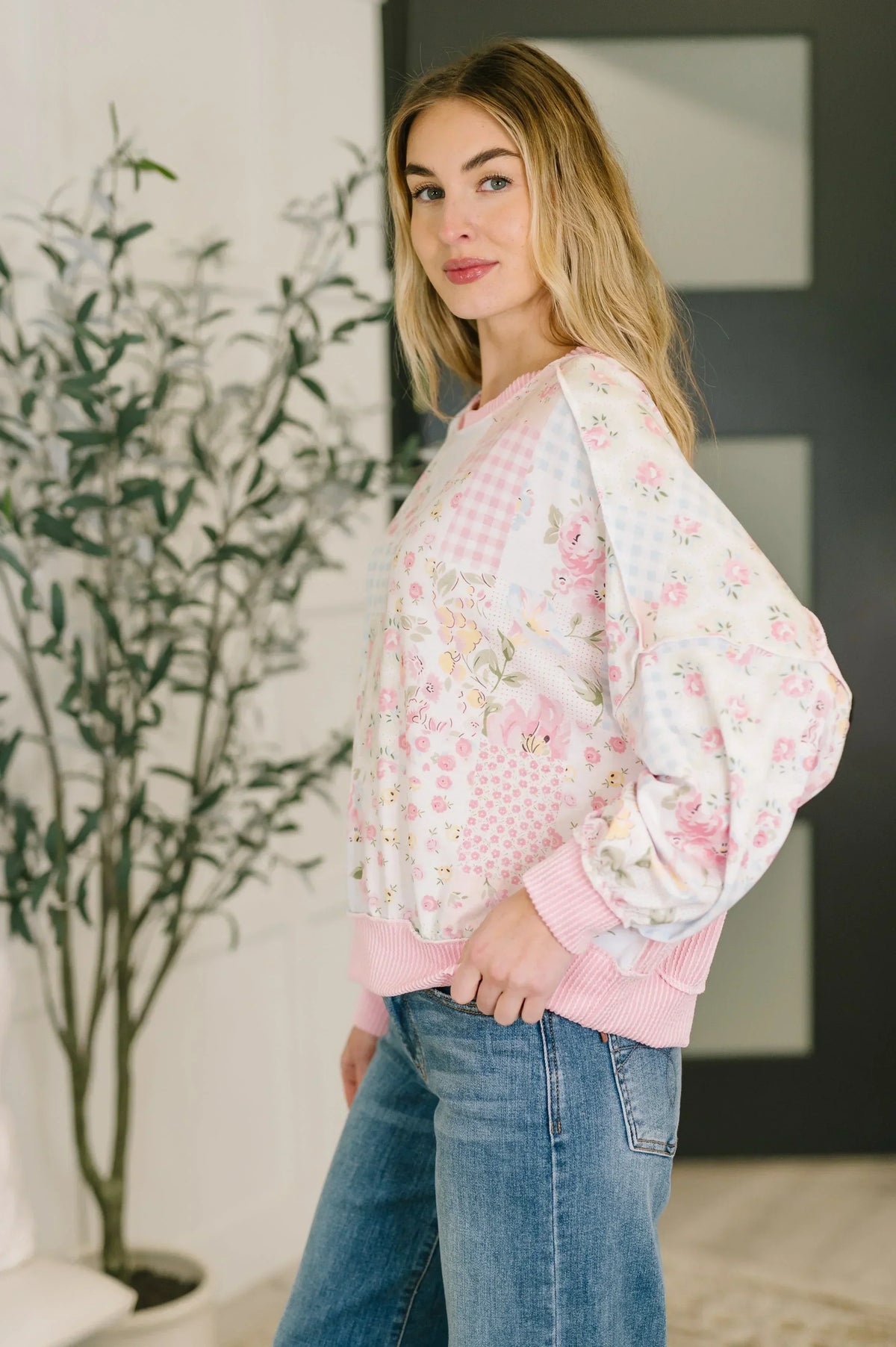 Woman wearing a floral patchwork top with balloon sleeves and blue jeans indoors