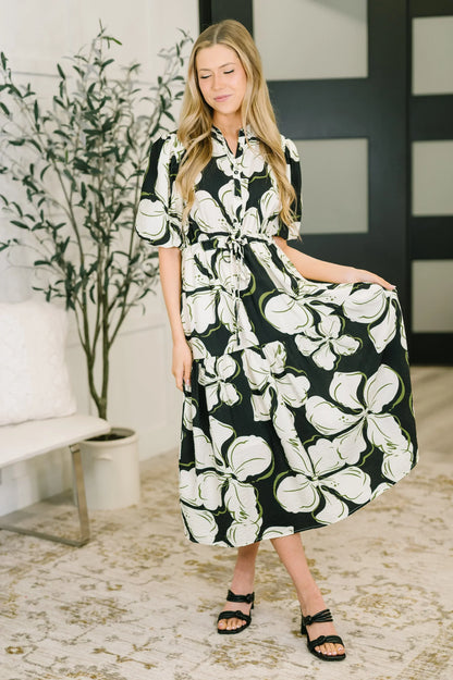 Woman wearing a black and white floral puff sleeve midi dress, standing indoors.