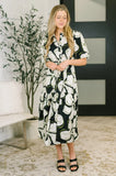 Woman wearing a black puff sleeve midi dress with white floral print, standing indoors