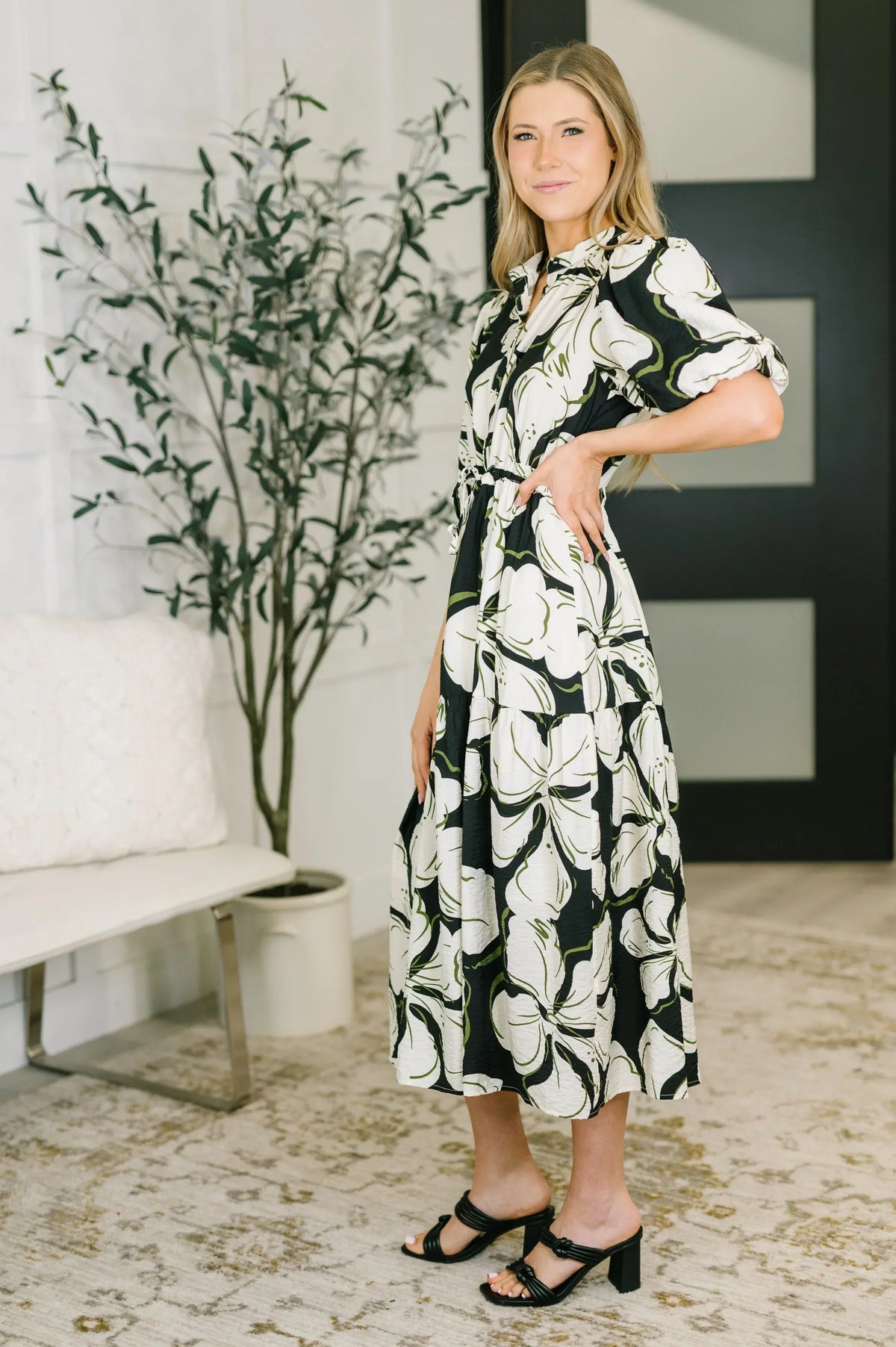 Woman wearing a black and white floral puff sleeve midi dress with sandals indoors