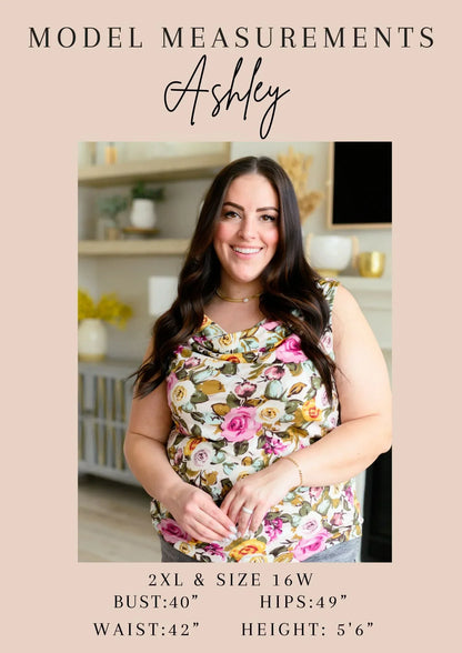 Woman with long dark hair modeling a floral sleeveless top in a bright indoor setting.