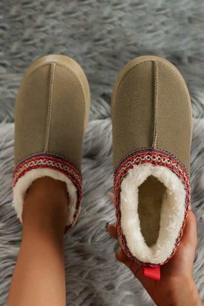 Cozy tan slippers with faux fur lining and red patterned trim on gray faux fur rug