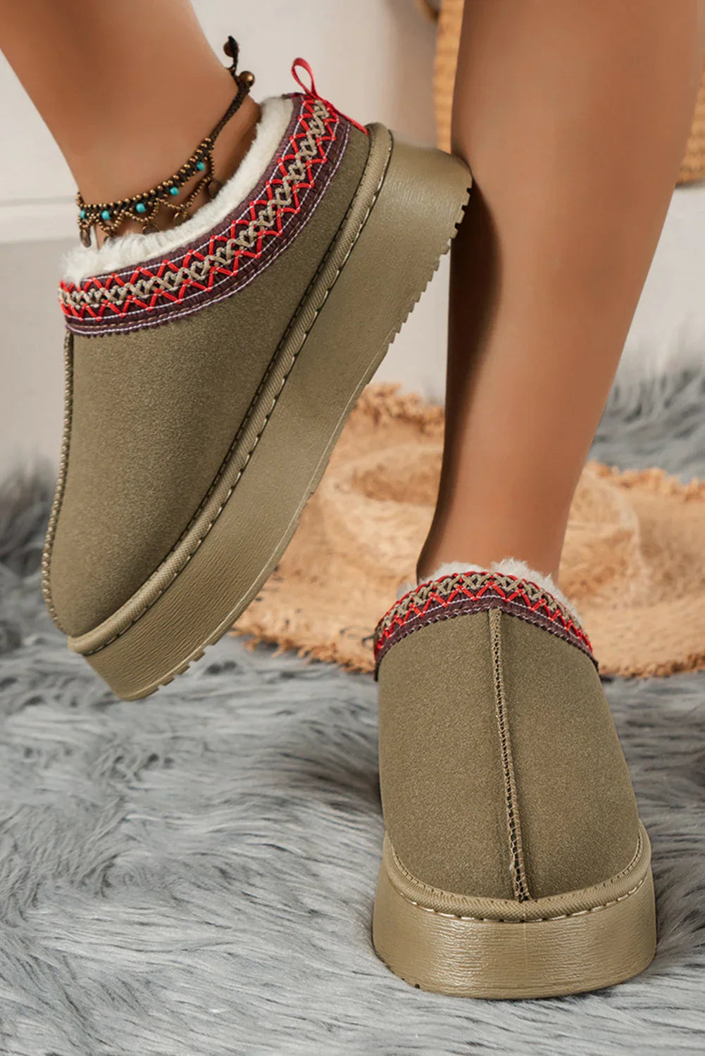 Olive green platform slippers with embroidered trim and faux fur lining on faux fur rug.