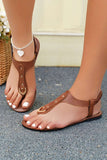 Woman wearing brown leather thong sandals with gold buckle detail and white nail polish
